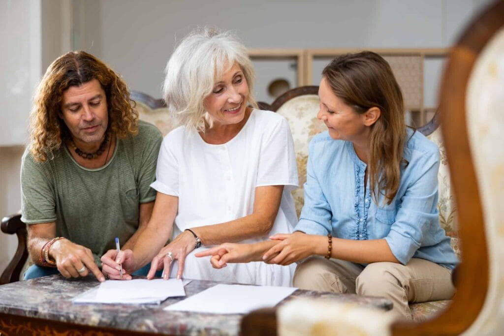 Three adults sit at a marble table, reviewing papers together and discussing.