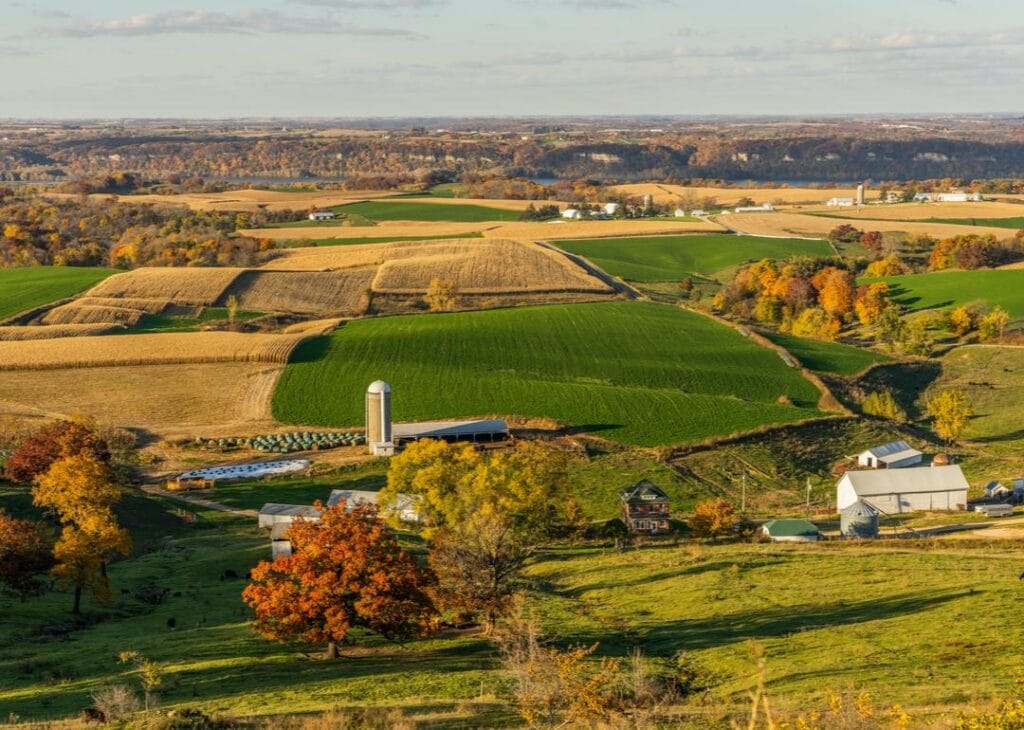 rual - Heartland Auction & Realty Group Rural farmland with patchwork fields, a silo, and farm buildings among autumn trees.